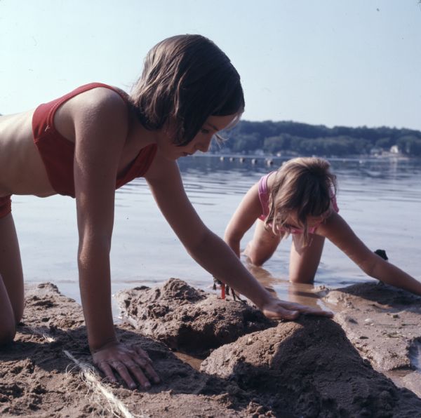Close-up of two girls playing in the wet sand on the shore of Long Lake.