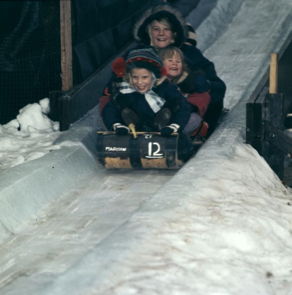 A woman and three children are tobogganing down a snow and ice ramp.