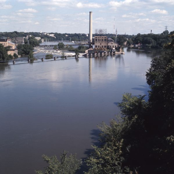 Elevated view over trees towards the Fox River. A dam is creating a reservoir for hydroelectric power. Former paper mills are on the left shore of the river.