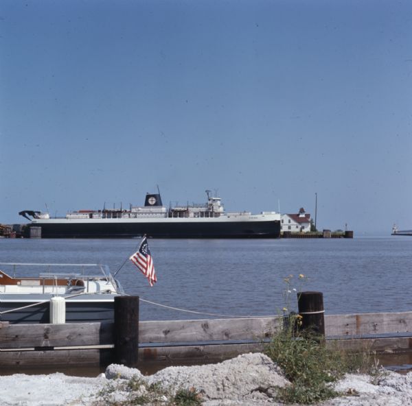 A cargo ship, the "Viking," is docked in a harbor. An American Yacht flag is attached to the back of a boat in the foreground.
