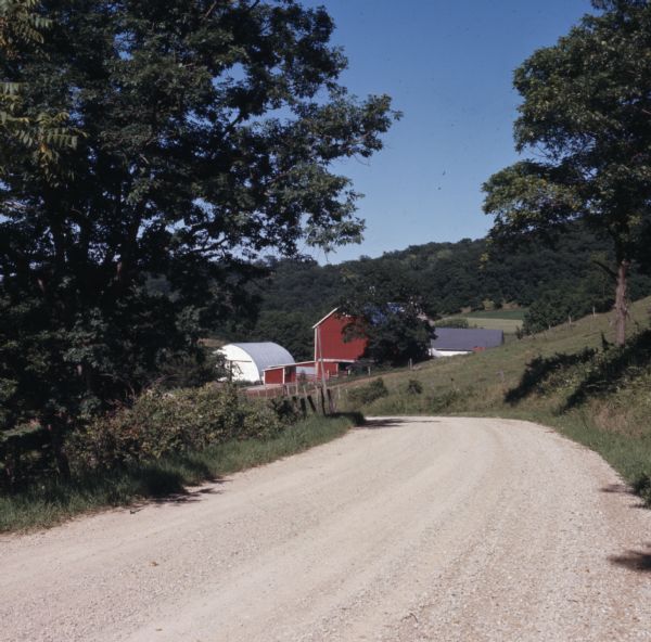 View down a gravel road leading down to farm buildings.