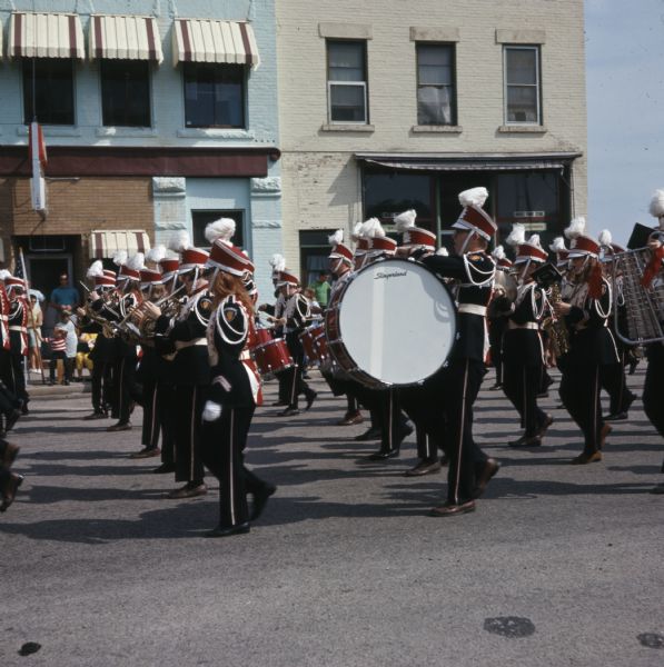 View from side of street towards a marching band playing as they march in formation down a street.