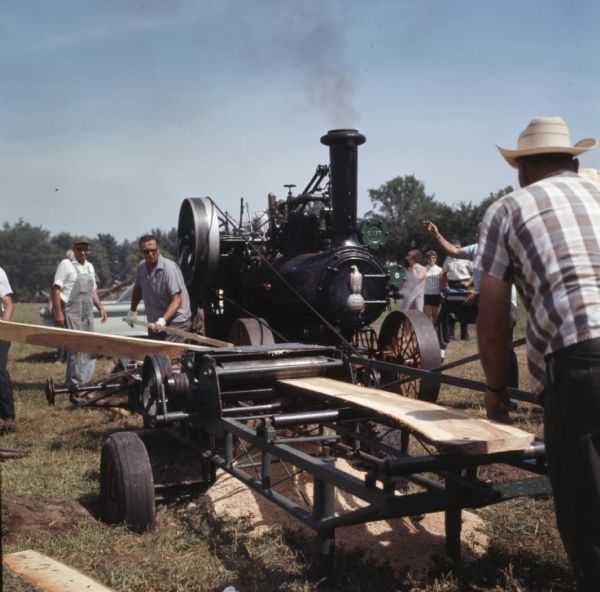 A group of men are using a steam powered tractor for belt-driving a planer for a demonstration at Steam Engine Days.