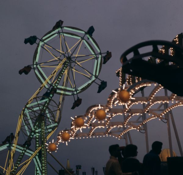 Green, yellow, and orange lights are illuminating carnival rides at night.