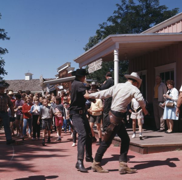 Two men, dressed in old western costumes, are pretending to fight each other for the entertainment of a crowd at Fort Dells.