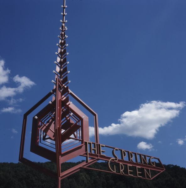 Close-up view of the entrance sign at The Spring Green. The sign is a metal sculpture which incorporates lights and geometric shapes.