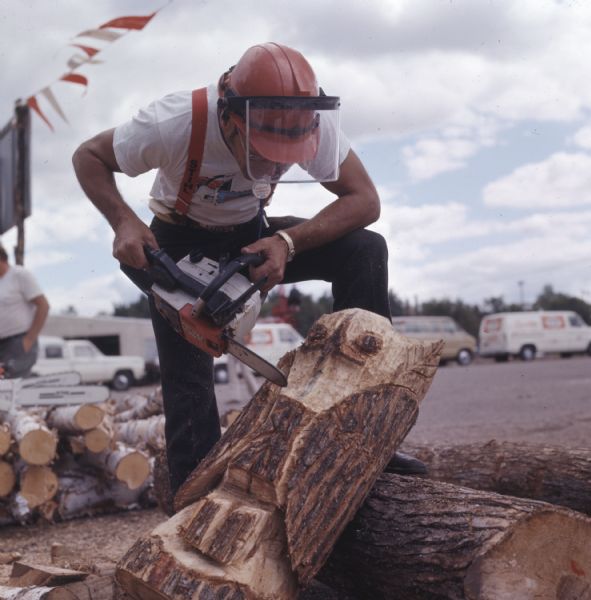 A man is bracing himself on a log while using a chainsaw to carve an owl out of a log.