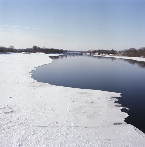 Elevated view of Wisconsin River. Snow and ice is covering part of the river, and in the distance is a bridge over the river.