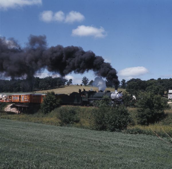 View across field towards a railroad train transporting circus wagons on open railroad cars.