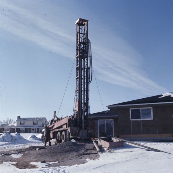 A man is operating a drill to create a well near a home under construction.