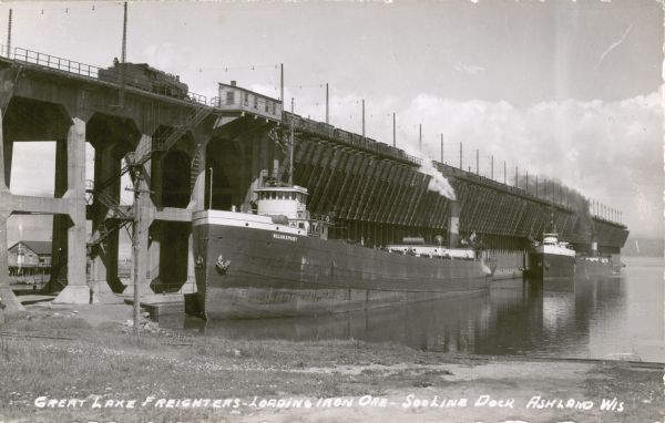 View from shoreline towards three ore boats at the Soo Line Railroad dock being loaded with iron ore. The first in line is the <i>William B. Pilkey</i>.