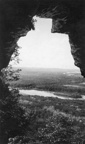 A retouched, elevated view, looking out the mouth of a cave, over Nelson Dewey State Park. Far below are a railroad bridge and the backwaters of the Mississippi River.  