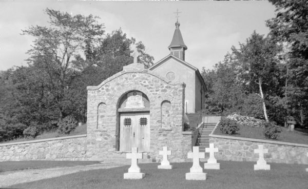 The tomb of Rev. Ambrose Oschwald (1801-1873), faced with fieldstone, is built into the hillside behind the Loretto chapel at St. Nazianz cemetery.  White stone crosses in the foreground mark the graves of Salvatorian priests who graduated from or were otherwise associated with St. Nazianz Seminary.  