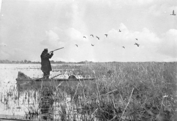 As described on the negative envelope, an unidentified man is standing in his boat, "Shooting at a flock of mallards at Lake Partridge near Fremont on the opening day of the duck hunting season."