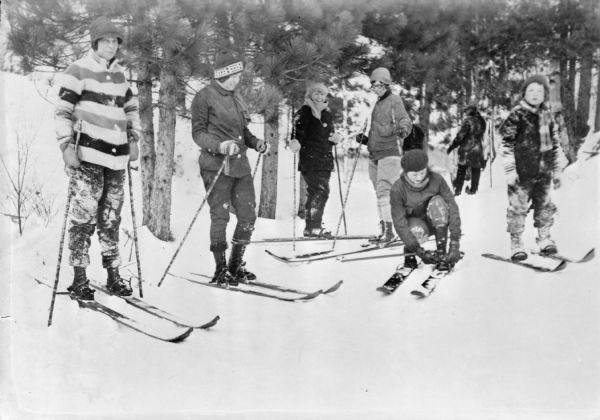 A group of skiers posing in front of a stand of small pine trees. The caption on the negative envelope reads: "Mrs. F.A. Marshall, Mrs. R. Becher, Mrs. Mary Mylrea, Mrs. Leadbetter, and Kneeland Pierson getting ready to ski."