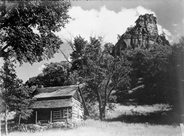 View looking up towards a log cabin near the base of a tall rock outcropping.