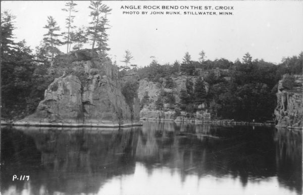 Photographic postcard view across water towards rock formations along the St. Croix River in Interstate State Park. "Caption reads: "Angle Rock Bend on the St. Croix.""
