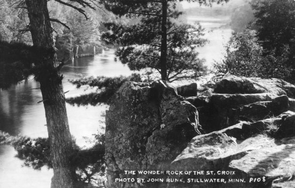 Photographic postcard elevated view of the St. Croix River in Interstate State Park, with a large rock outcropping and pine trees in the foreground. Caption reads: "The Wonder Rock of the St. Croix."