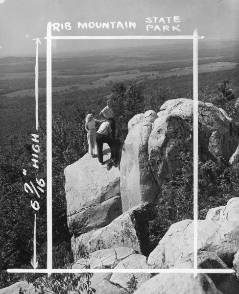 In this photograph marked for cropping for publication, a group including a young woman, two young men and a boy observe the features of a rock outcropping from a precarious high perch on Rib Mountain.  Woods and fields are visible in the distance.  