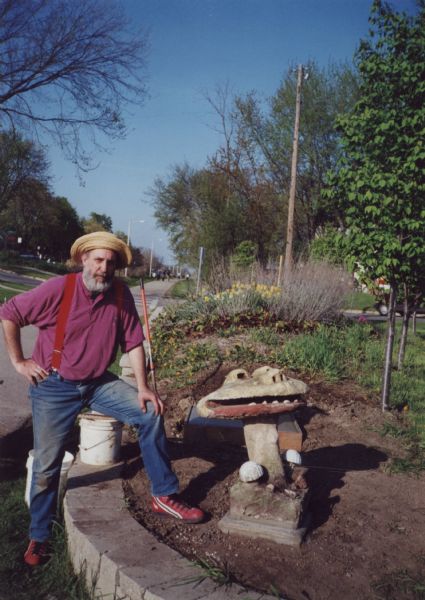 Lou Host-Jablonski, AIA architect, standing by the "Smiling Mushroom" and a new concrete foundation that he poured for the "Blue Dragon Urn." Both sculptures are from Sid Boyum's backyard and were relocated to the public green space on the bike path at Atwood Avenue and Dunning Street. The freshly installed square foundation is behind the "Smiling Mushroom." Daffodils are in bloom in the background with other spring bulbs.  The sculpture relocation and public installation was a community-based, volunteer project to preserve Boyum's larger outdoor work to public parks, landscaped areas and private residences throughout the Atwood-Schenk neighborhood.