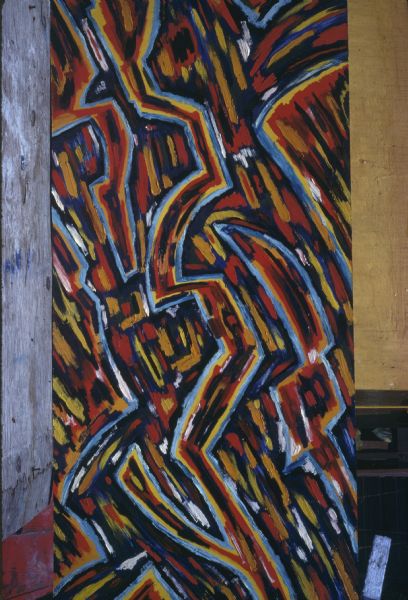 Photograph of an original oil painting on canvas by Sid Boyum titled "Traffic." The work pictures a multi-colored abstract piece displayed vertically against yellow and gray walls. 