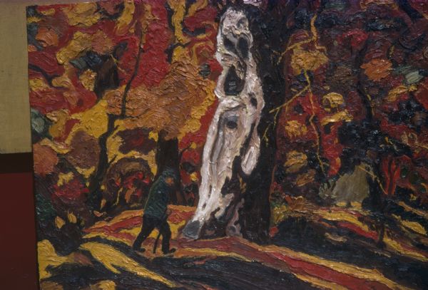 Photograph of an original oil painting of an autumn scene by Sid Boyum. The work shows a small, solitary man in dark greenish hat and coat using a walking stick in a forest of brightly colored fall trees, ablaze with swirling reds, oranges, yellows and browns. He is seen approaching a large, burled trunk that is centrally highlighted in whites and grays. The circular brushstrokes of foliage contrast with the linear brushstrokes of the forest floor. The heavy application of paint adds to the canvas surface texture. The canvas is propped against a yellow and red wall. 