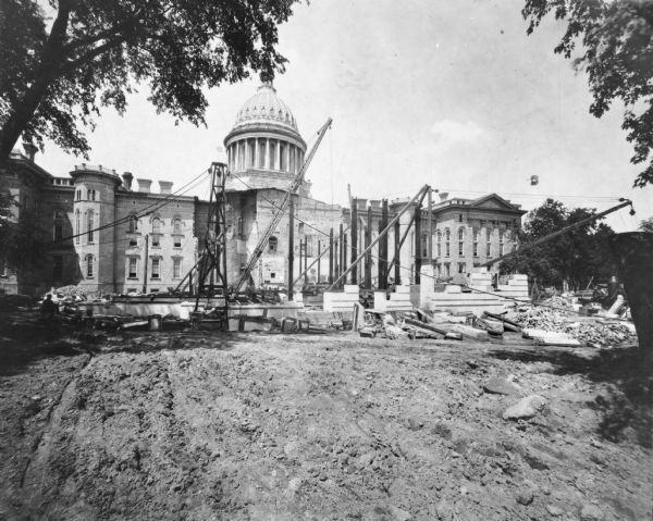The construction of the East Wing of the new Capitol is underway. This is a view of the North and South Wings and the dome of the Third Wisconsin State Capitol. On the far left is the best known view of the way in which the architect had joined the Third Capitol with its 1883 addition.