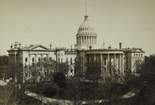 Elevated view of the Wisconsin State Capitol. The north and south wings were added in 1882-1884. The trees in the park are not yet full of leaves and did not obstruct the view. As a result, the curvilinear walkways can be seen. The Capitol Park was designed by noted landscape architect Horace W.S. Cleveland, but his design was only partially developed. This photograph is oriented with the North Wing addition at the left.