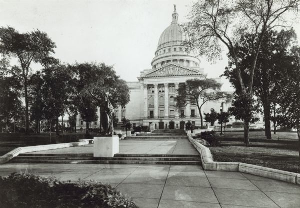View up sidewalk towards the Wisconsin State Capitol, with the North Pediment, called "Learning of the World, by the sculptor Attilio Piccirilli, just below the dome. In the foreground at the top of three steps is the the "Forward" statue created by Jean Pond Miner.