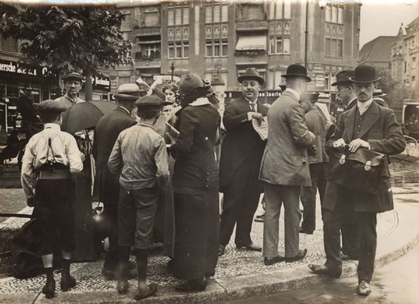 A group of people on a sidewalk in Berlin during the mobilization period in August 1914. Extra editions of newspapers with the latest war news are being distributed.