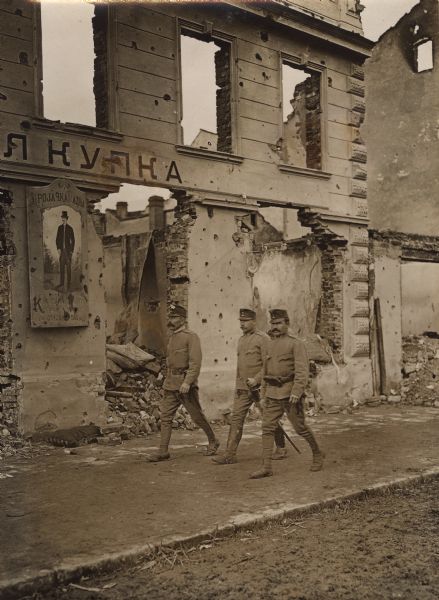 Three Austrian soldiers walking past a damaged building in Valjevo, Serbia.