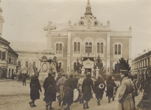 Soldiers are strolling through the square, with some of the men carrying musical instruments. In the background is the Bishop's Palace.