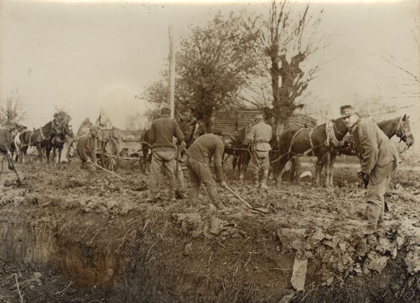 Soldiers repairing a road on the way to the front in World War I. Horse-drawn wagons are in the background.