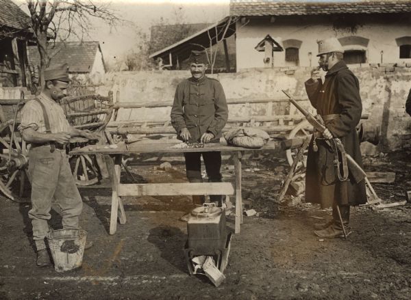 Soldiers are standing around while a cook is working at the outdoor field kitchen on the front during World War I.