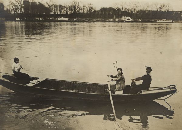 An Austrian sailor and a woman are rowing a boat in the Danube River during World War I. Another woman is sitting in the front of the boat.