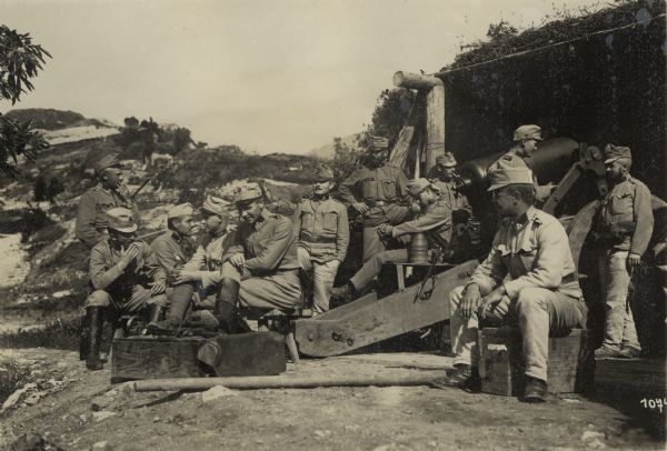 Austrian artillerymen taking a break from the battle at a firing position on the southwestern battlefront in Tyrol. Some of the men are smoking. The troops are resting in a firing position awaiting the order "Make ready to fire."