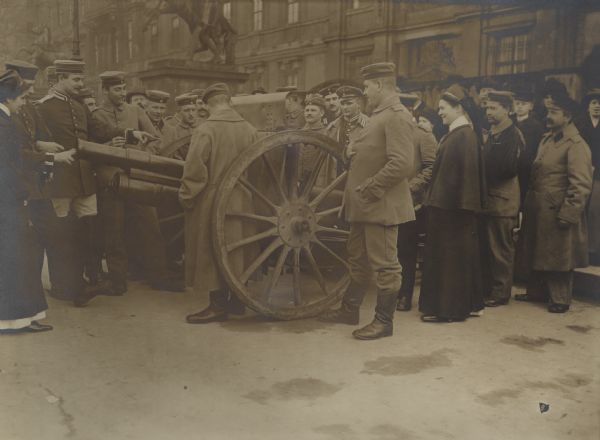 Wounded soldiers, and nurses, standing outdoors examining a captured artillery piece. 