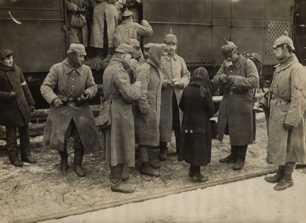 German soldiers standing on a platform near a stopped troop train buying refreshments from a young girl. 