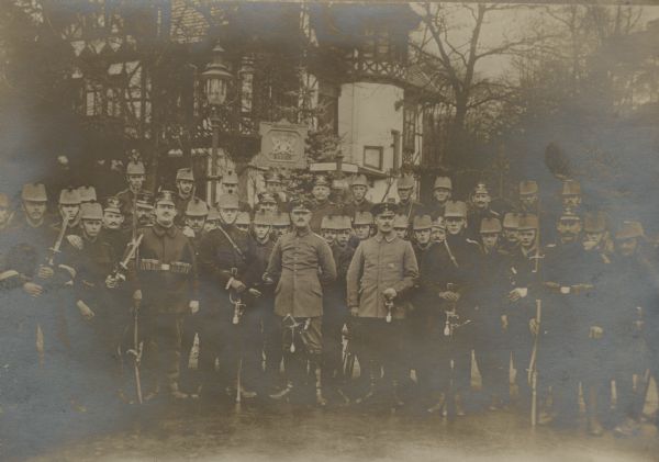 Group portrait of border guards on the Swiss frontier. A large building among trees is in the background.
