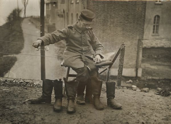 Military cobbler repairing boots. Buildings are in the background.