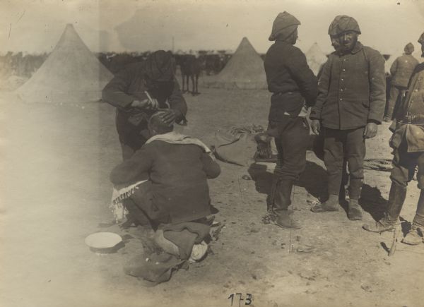 Turkish barber at work in camp shaving the head of a fellow soldier.