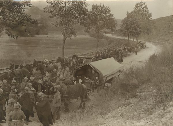 Elevated view of people gathered on a road. There are railroad tracks alongside the road on the left. Our Bavarians in the Vosges. The welcome sutler wagon.