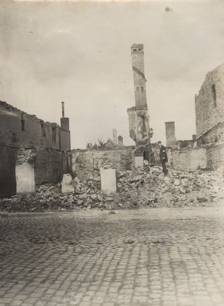 Scene of destroyed and burned buildings. A man is standing on top of a pile of rubble.