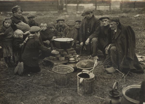 Belgian refugees sitting around a fire, eating soup.