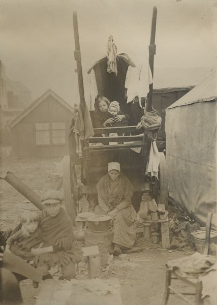 Refugees posing in front of their wagon and their huts as they are preparing for another long, hard day.