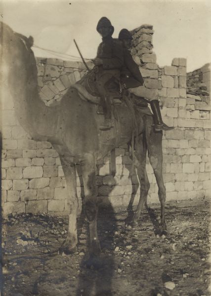 Two soldiers riding a camel to the front. 