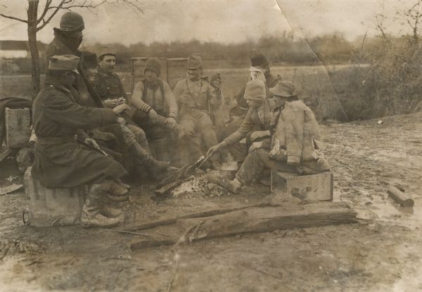 Sitting around a campfire in Serbia. Austrian soldiers and civilians are gathered around a fire. 