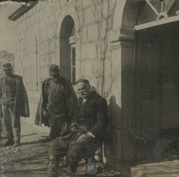 After the downfall of Montenegro in the Town of Njegusi, the summer residence of King Nikita. A kavass (armed guard) of the king is sitting in front of the main entrance. 