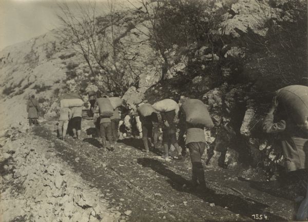 Repair work on Mount Lovcen to repair roads. Civilians carrying bags of cement up a road to the repair site. 