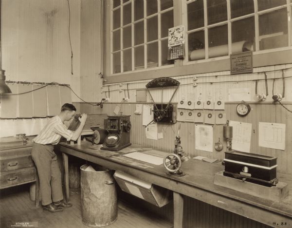 View of an unidentified male scientist looking into boxed paper apparatus, surrounded by other measuring tools and scales, in the corner of a Kimberly Clark testing station laboratory.  